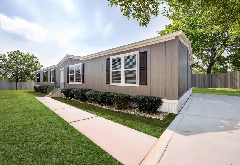Exterior view of the Navasota 3272H mobile home for sale by Champion Home Builders, offered at Valley Homes, showcasing a beautifully landscaped yard and contemporary design.